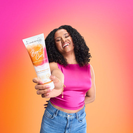 Smiling woman with curly hair holding Boost Curl hair gel on pink-orange gradient background