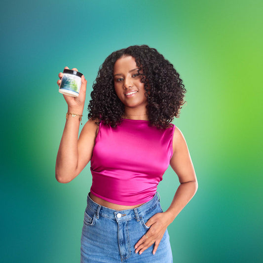 Smiling woman with curly hair holding natural hair care product against green background