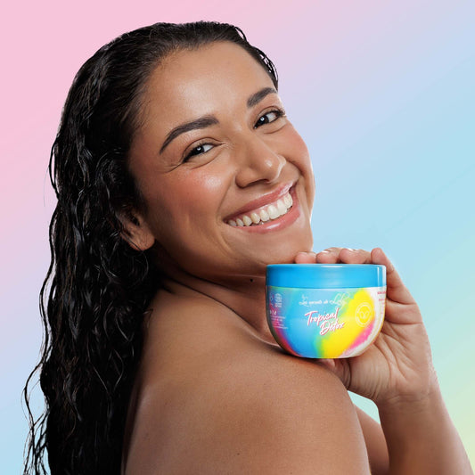 Smiling woman with wet wavy hair holding Tropical Detox hair care product