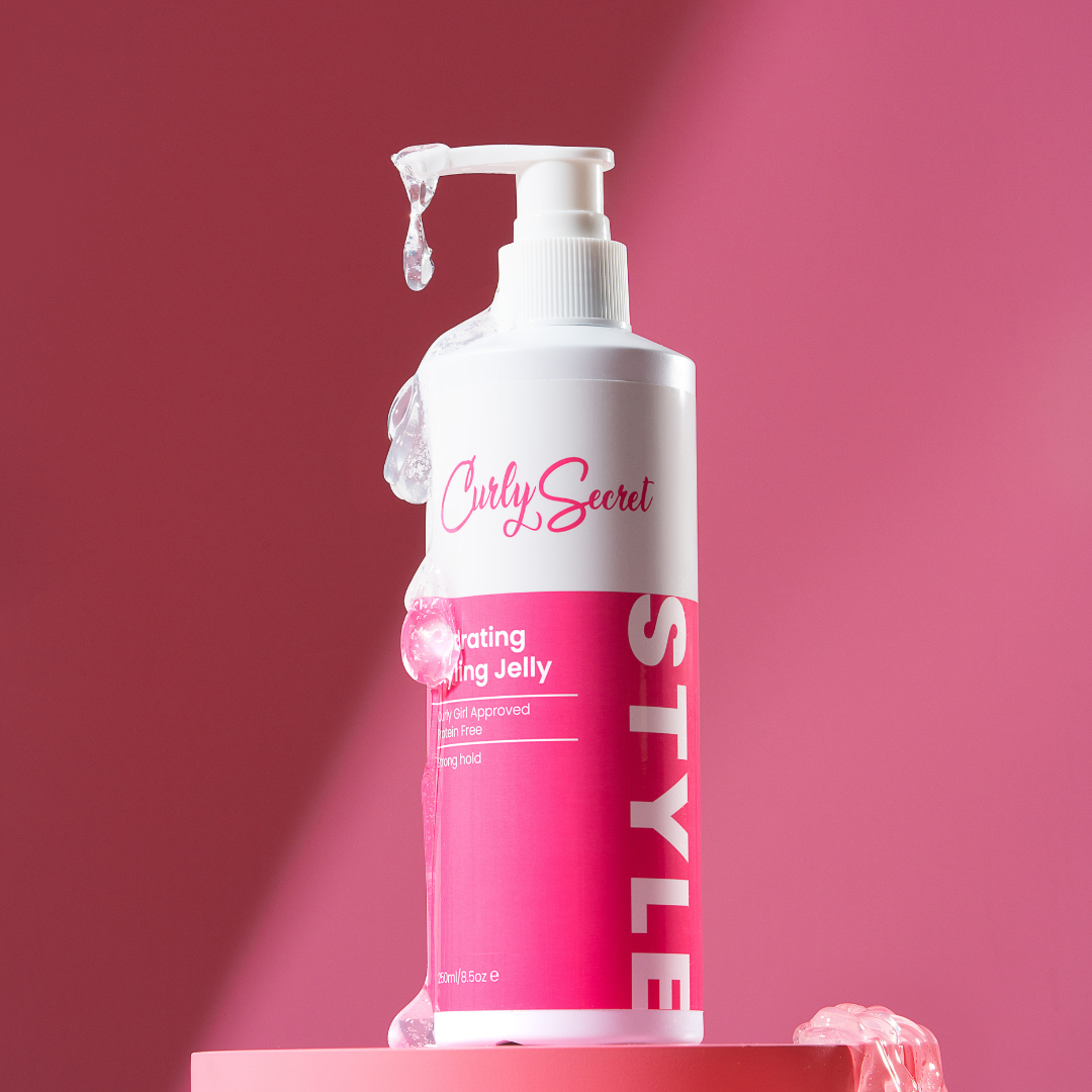 Hydrating styling jelly for curly hair in a pump bottle with pink label on pink background
