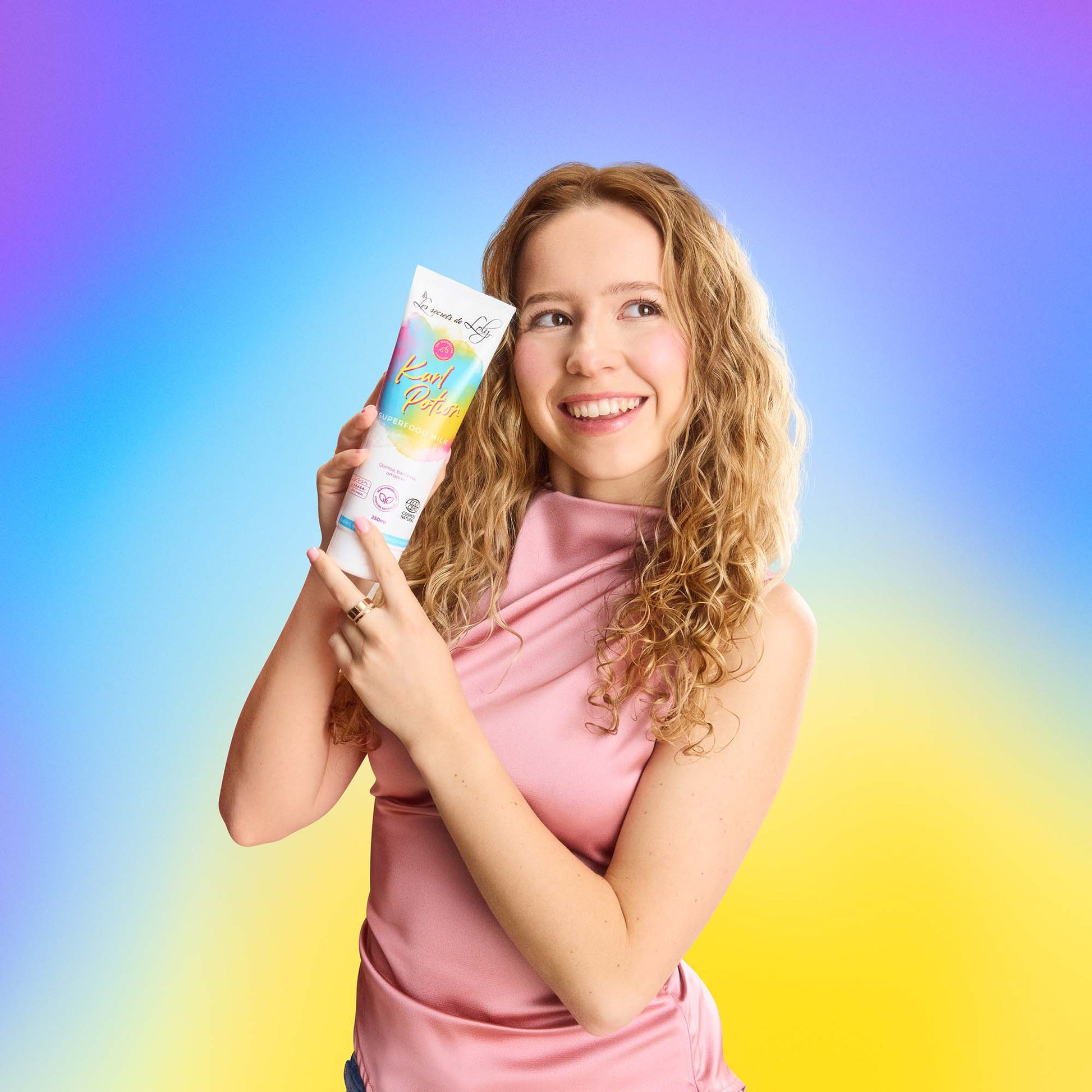 Smiling woman with curly hair holding curl cream for natural hair care against colorful background