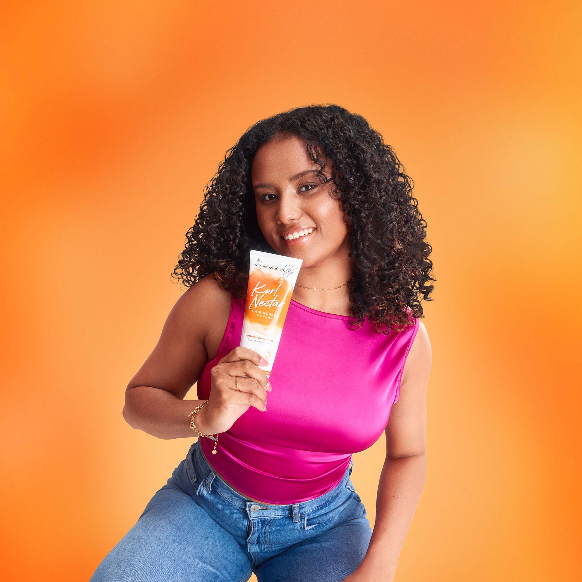 Woman with curly hair holding curl cream tube on orange background, hair care concept